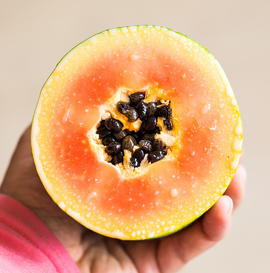 Hand holding papaya — a natural ingredient with fruit enzymes for skin found in glowoasis vegan probiotics exfoliating powder.