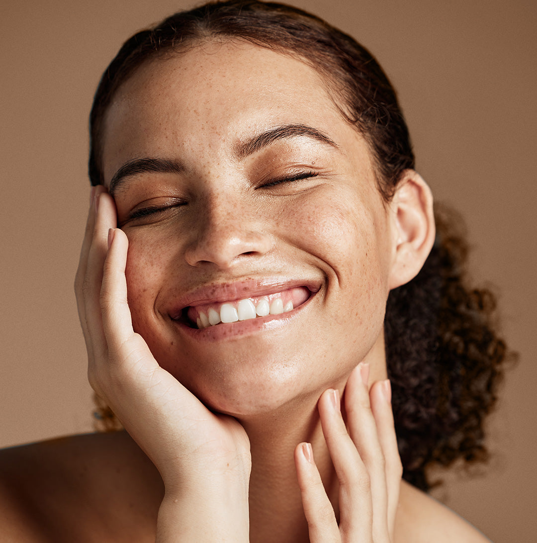 Smiling female with eyes closed feeling her skin after using vegan probiotics for skincare.