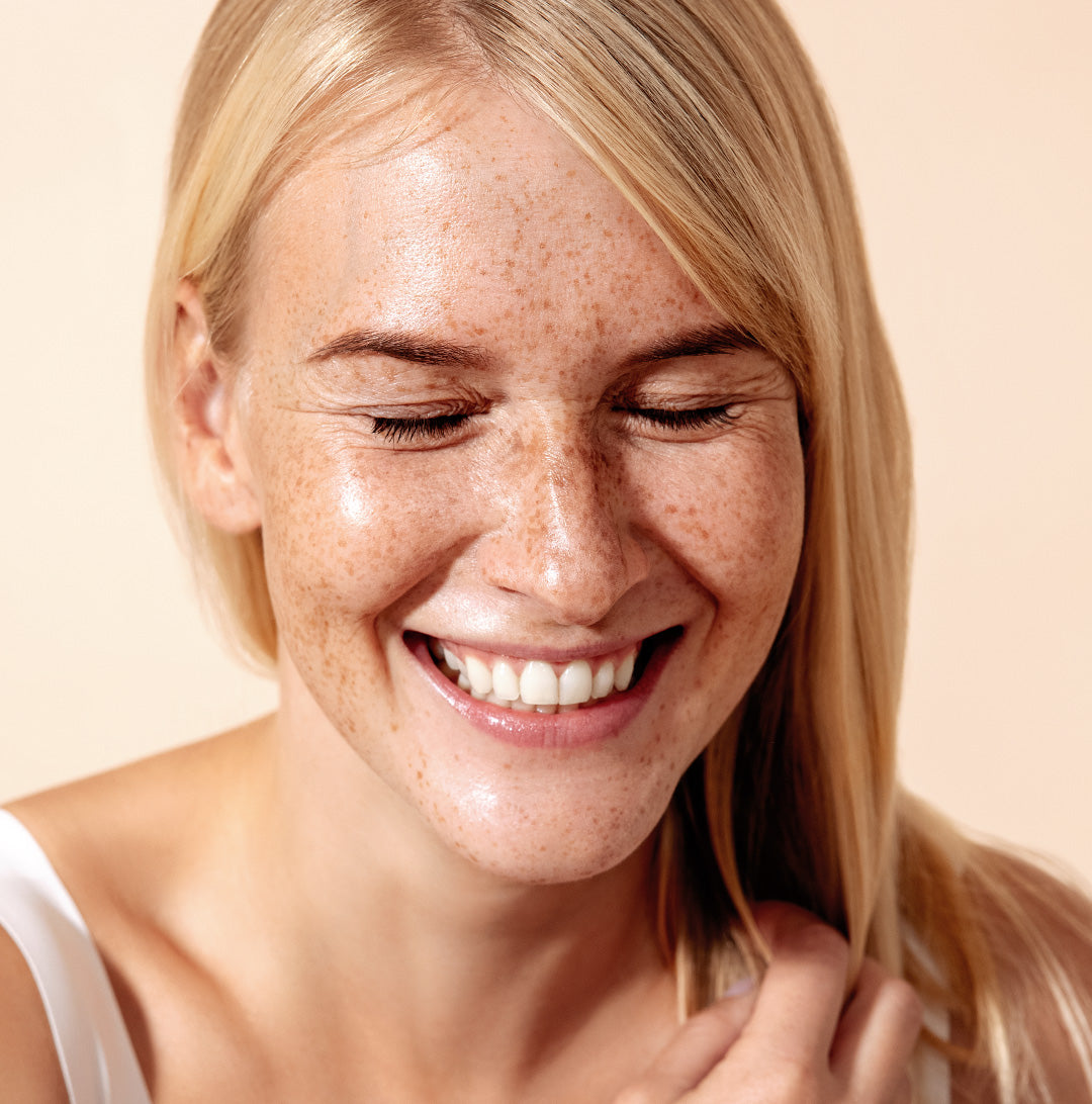 blonde female with freckles smiling with her eyes closed