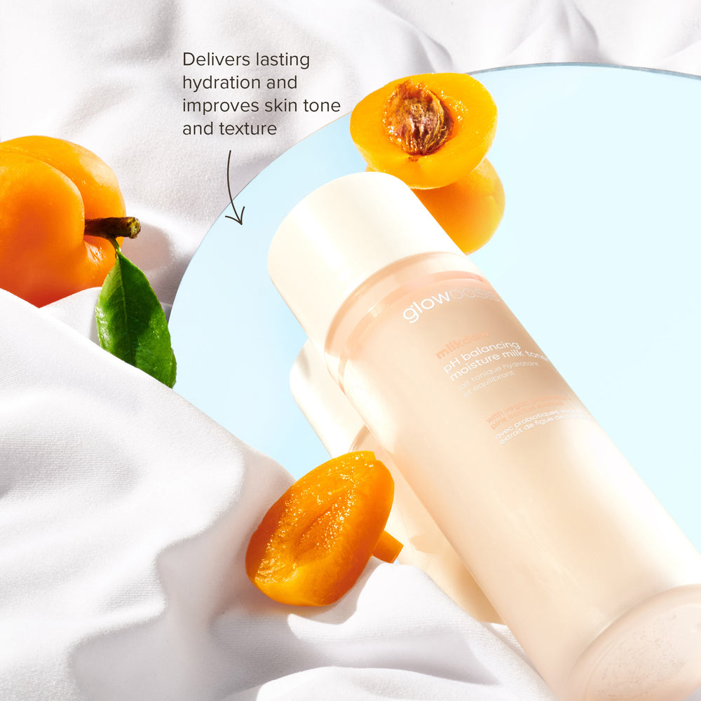 glowoasis vegan probiotic milkdew pH balancing toner laying on a mirror with apricots scattered nearby.