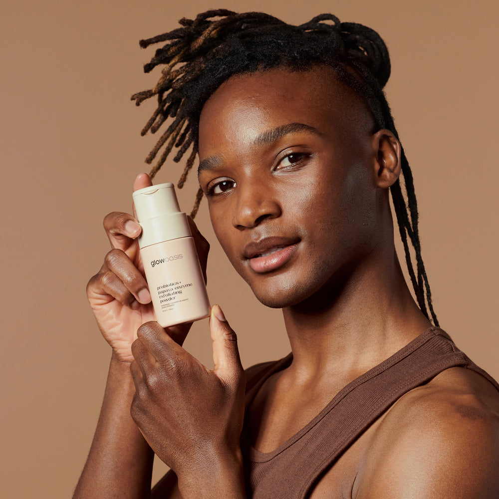 Male holding glowoasis vegan probiotics + papaya enzyme exfoliating powder next to his face.