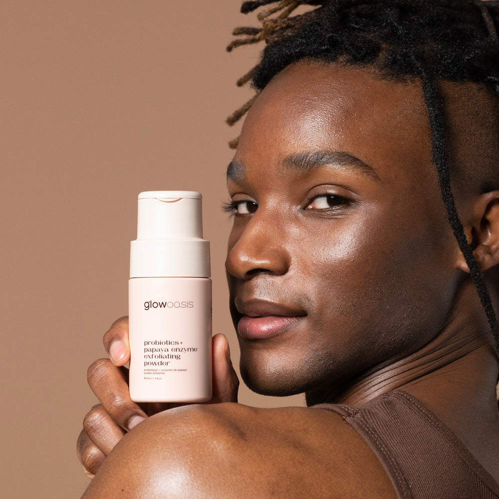 Male holding glowoasis vegan probiotics + papaya enzyme exfoliating powder above his shoulder.