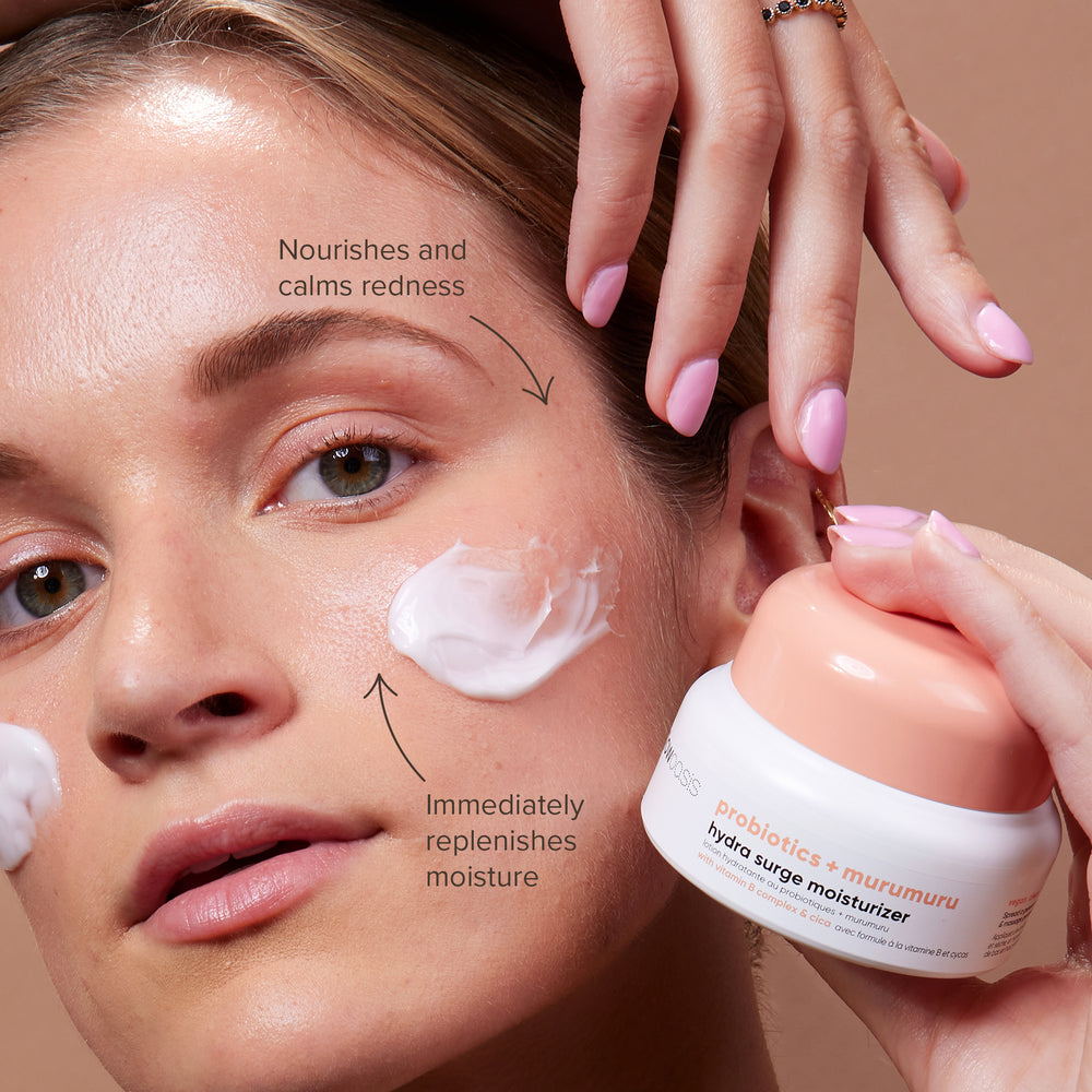 Female model with glowoasis vegan probiotics hydra surge moisturizer cream applied to cheeks while holding up the container to show that the product plumps, nourishes, and replenishes moisture.