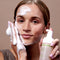Female model with glowoasis vegan probiotics cloudcleanse cloud whipped gentle daily foam cleanser applied on cheeks and forehead while holding sustainable dispenser in hand.