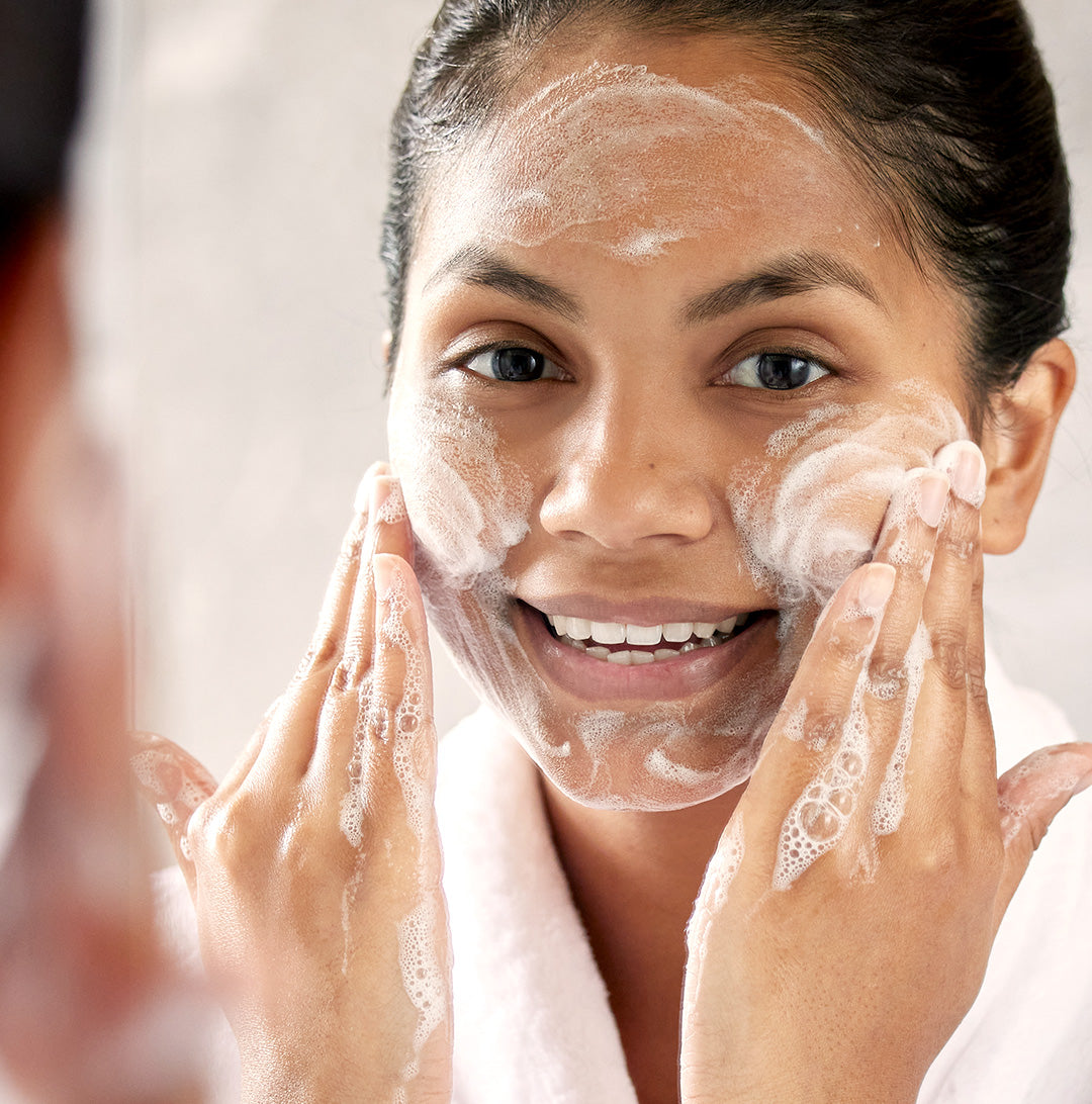 Woman in a white robe gently cleansing her face with vegan probiotic skincare for a healthy glow.