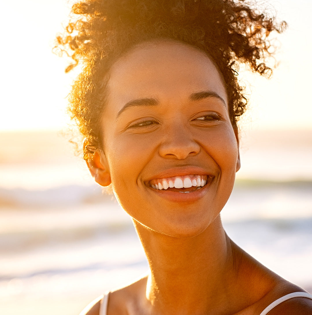loseup of woman smiling on a beach with a healthy glow.