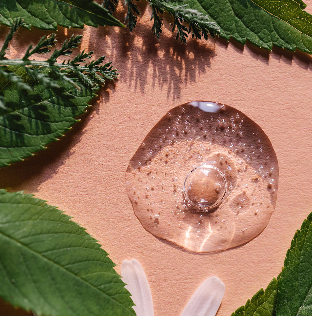 Vegan probiotic skincare texture shot on peach-colored background surrounded by leaves. 