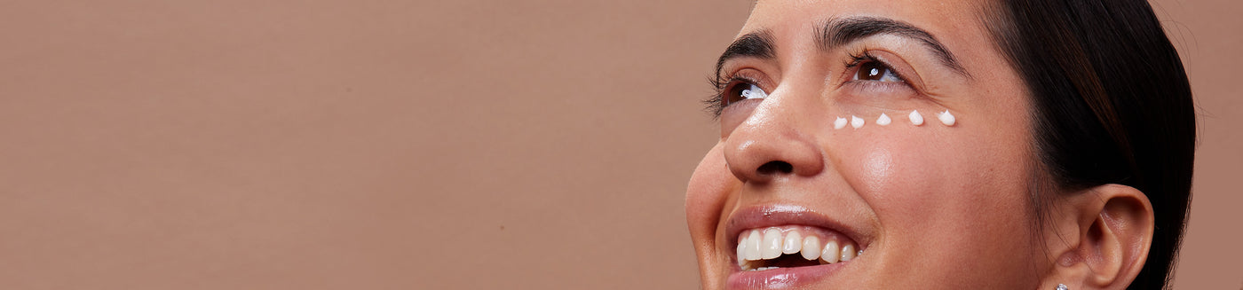 Smiling female model that has glowoasis vegan probiotics anti aging triple peptide refreshing eye cream applied underneath eye.